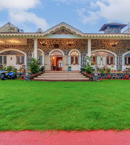 Charming stone bungalow in Lonavala with arched entrances, lush green lawn, and colonial-style architecture