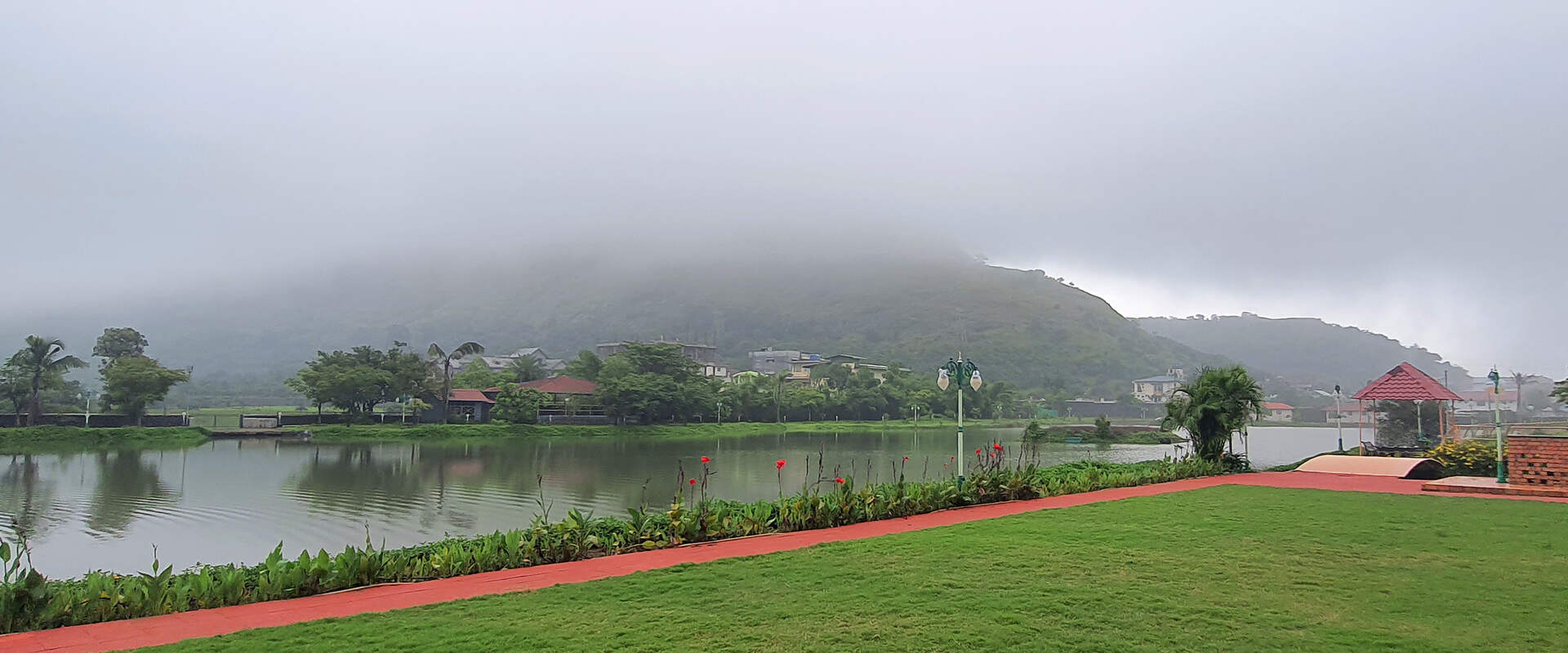 Private luxury villa in Lonavala with lush green lawn, lakeside view, and peaceful foggy mountain backdrop